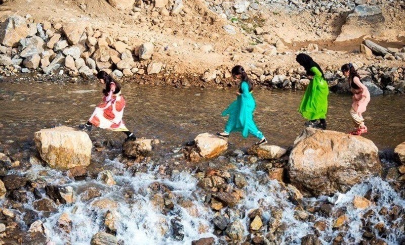 کودکان با لباس‌های محلی رنگارنگ خود در حال بازی در رودخانه هستند