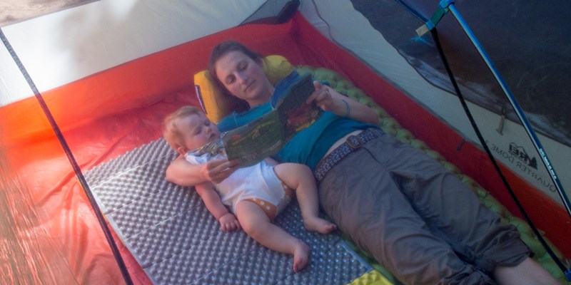بچه‌ای در کمپ که به آرامی در بغل مادرش دراز کشیده و کتاب می‌خواند!